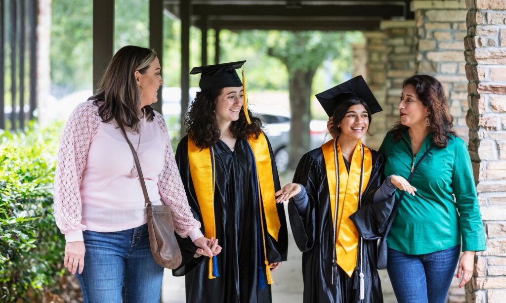 Two high school graduates with their mothers, talking